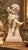 An elegant statue of a winged cherub (putto) seated on a louis xvi neoclassical pedestal. The cherub is depicted holding...