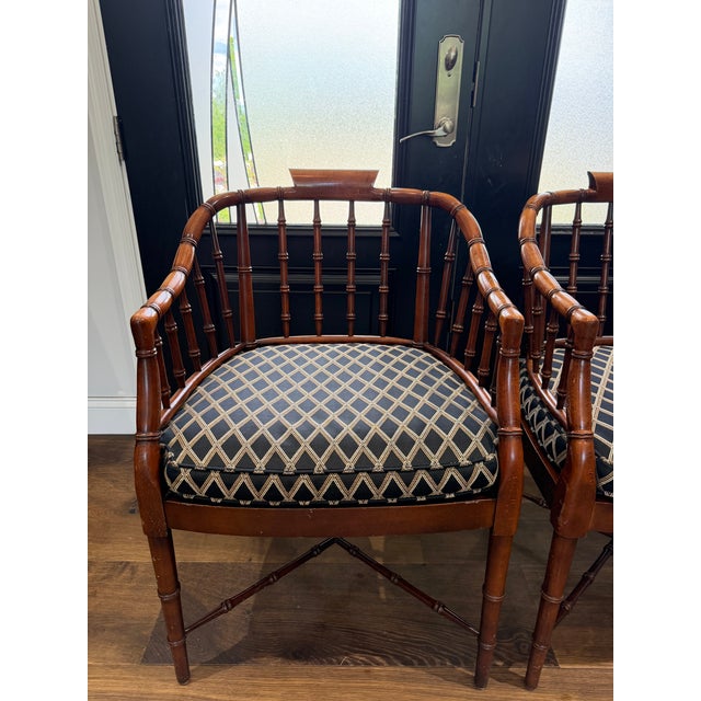 A refined and highly sought-after pair of vintage Baker Furniture faux bamboo barrel back armchairs, masterfully crafted...