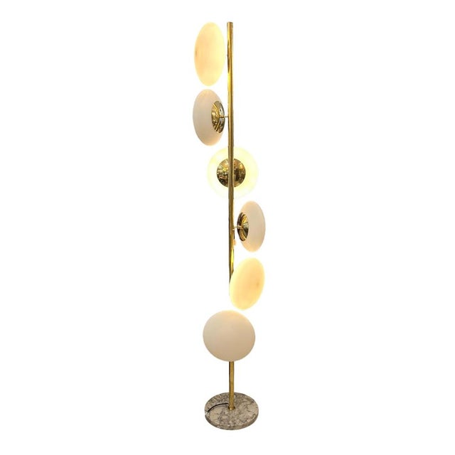 Italian floor lamp. It features a long, slender body in gilt brass, around which six matte white shades are arranged in a...