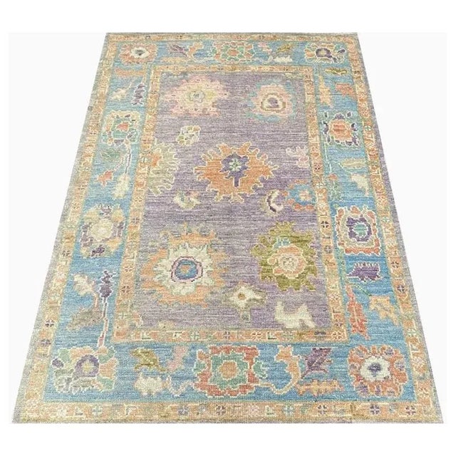 This traditional handwoven Turkish rug features a recreated antique Oushak design. The elegant purple field contains a...
