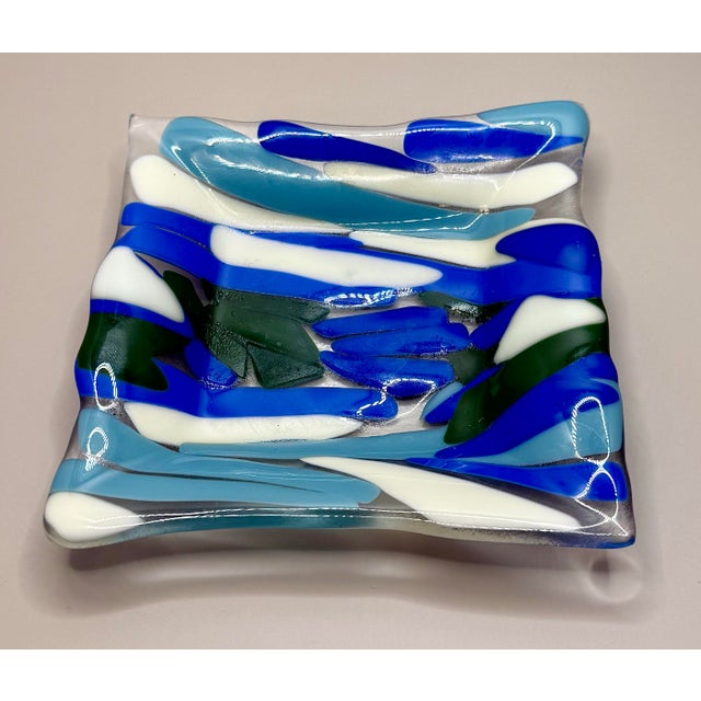 Contemporary Fused Glass Art Dish in Coastal Blues A striking artisan fused glass dish featuring layered ribbons of blue,...