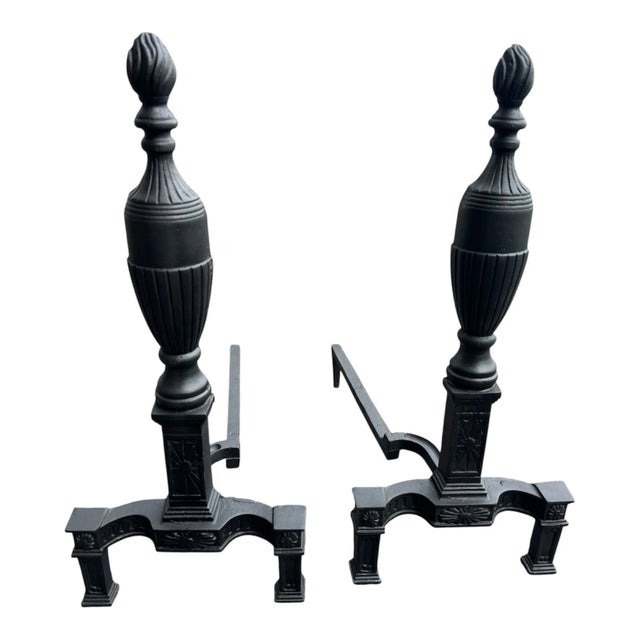 Vintage pair of cast iron fireplace andirons in elegant Neoclassical style, featuring classic urn finials and decorative...