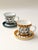 Hand-painted ceramic coffee cup and saucer, featuring abstract human face motifs rendered in line art. The design is...