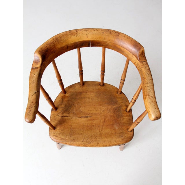 An antique Windsor captain’s chair with a graceful low, wraparound back, turned spindle supports, and a shaped wooden...