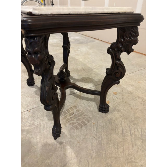 An American Rococo Revival parlor table featuring a rectangular white marble top and ornately carved walnut legs with...