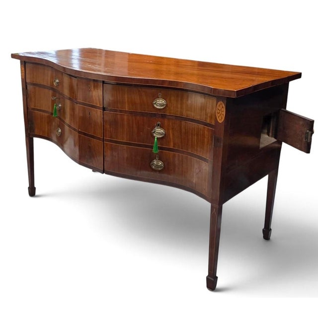 An exceptional and highly sophisticated English George III Hepplewhite serpentine sideboard, handcrafted circa 1790–1805...