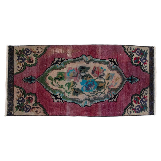A richly aged Ghiordes village piece with a wine-raspberry field and a soft ivory floral medallion that reads both...