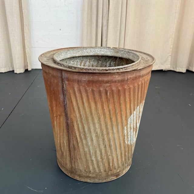 This rustic industrial bin showcases a raw, sculptural silhouette defined by its deeply corrugated, ribbed steel...
