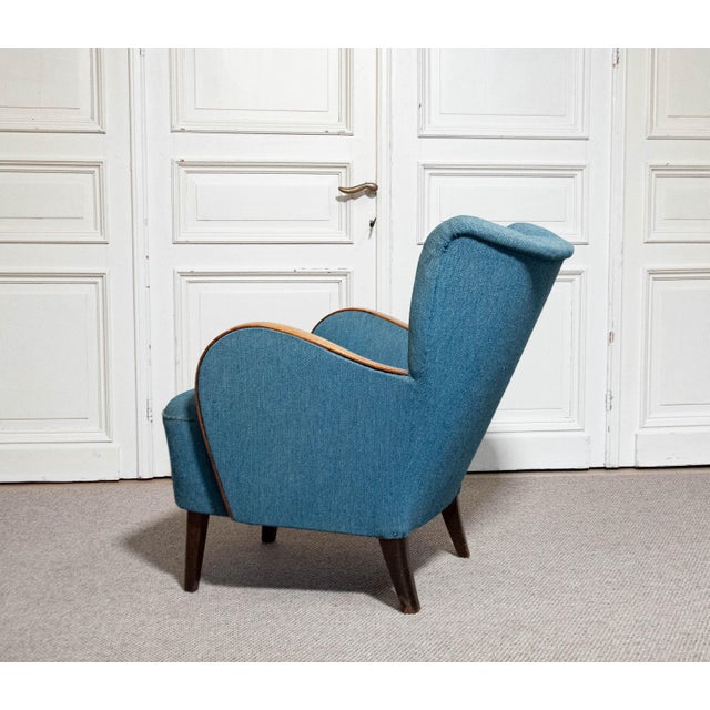 This is a Swedish Art Nouveau armchair from the 1940s, featuring a padded backrest and curved wooden armrests, adding an...