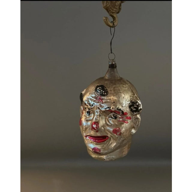 A hand-blown, silvered glass clown-head ornament from 1920s Germany, notable for its larger size and expressive molded...