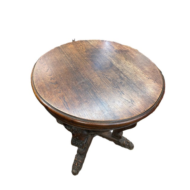 Heavily carved round oak side table characterized by figural supports like winged cherubs and feet shaped like grotesque...