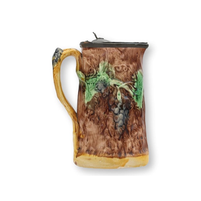 A charming late 19th century English majolica syrup pitcher modeled as a tree trunk with applied grape clusters and vine...