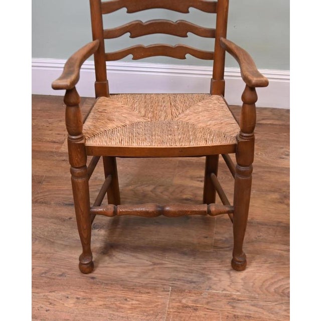 A charming harlequin pair of country ladder-back armchairs Each chair has six shaped back rails, gently curved arms and a...