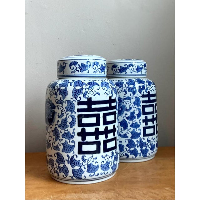 This pair of vintage Asian lidded urns presents a classic cylindrical silhouette, with softly rounded shoulders rising to...