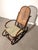 Elegant antique bentwood rocking chair featuring a sculptural dark-stained wooden frame and traditional woven cane seat...