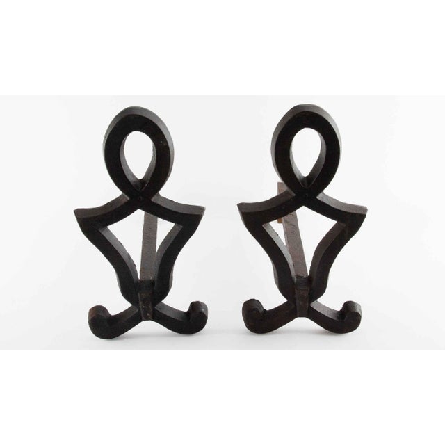 A pair of wrought iron andirons featuring stylized openwork standards with scrolling feet and circular ring finials. The...