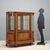 Display cabinet veneered in mahogany and walnut burl with ebony and maple trim. Central door and curved sides with beveled...