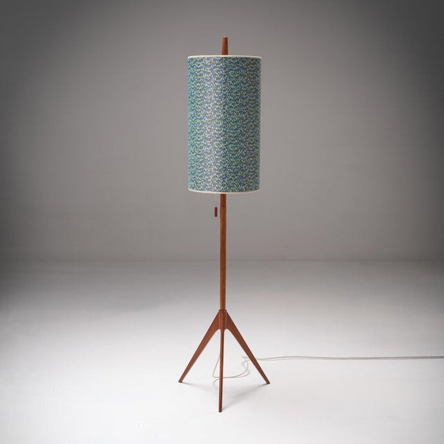 A sculptural Scandinavian floor lamp in warm teak wood, set on a refined tripod base. Its slim, architectural silhouette...