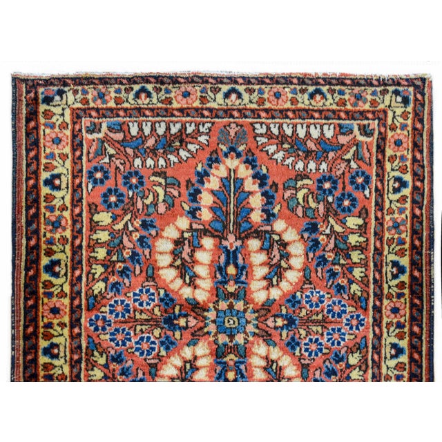 A charming early 20th century Persian Sarouk rug with a mirrored floral pattern woven in myriad colors against a coral...