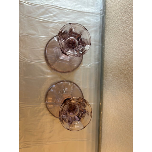 This vintage pair of amethyst glass candle holders with a pinkish tint, which is a common characteristic of glass made...