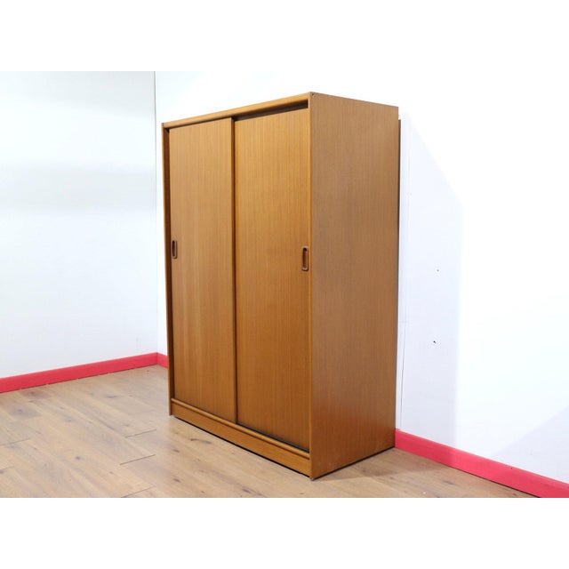 A beautiful British armoire with sliding doors, this Mid Century Modern Vintage Teak Sliding Door Armoire Wardrobe in the...