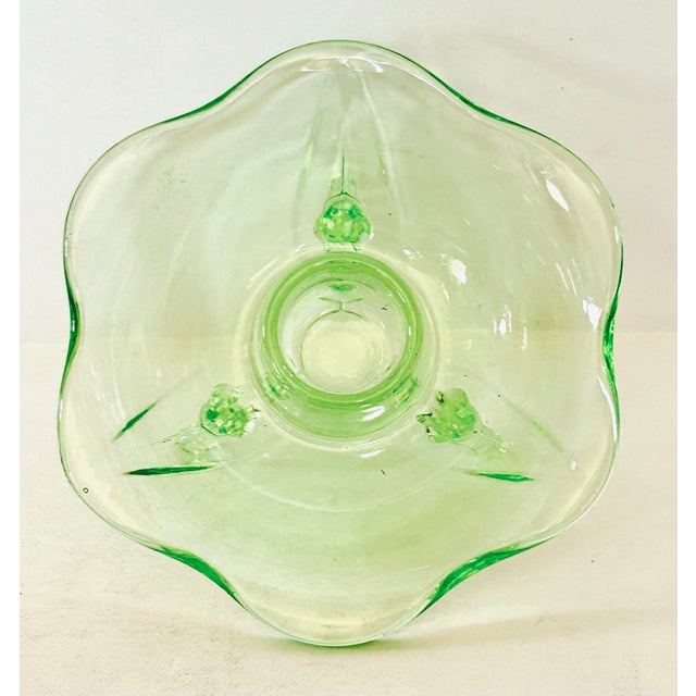 Vintage Fostoria candle holders are crafted from green uranium glass. Three-footed base with a scalloped, bowl-shaped top...
