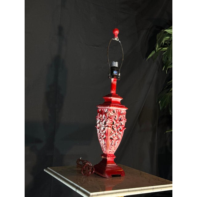 Description A bold decorative table lamp base featuring an ornate openwork form and distressed red finish. The sculptural...