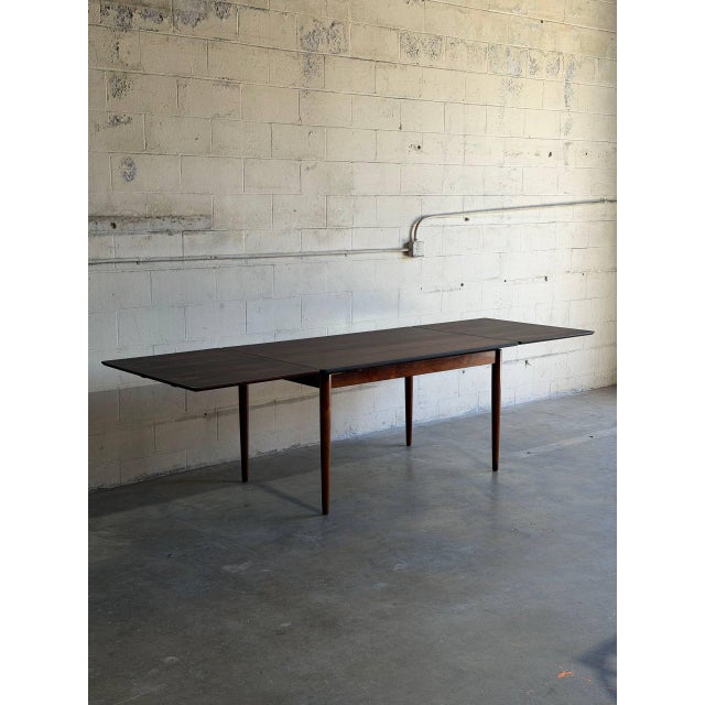 This minimalist wooden dining table features a clean rectangular top that smoothly expands with two pull-out leaves to...