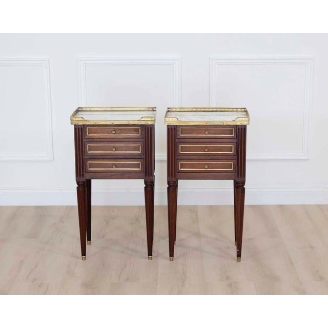 Made in France in the twentieth century, this pair of Louis XVI style bedside in wood veneer, each opening with three...