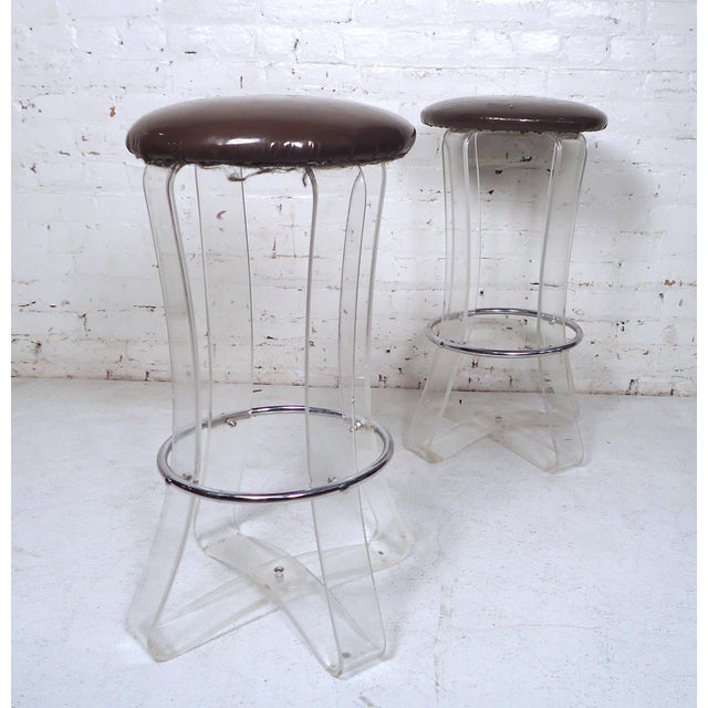 Unique pair of Mid-Century Modern Lucite stools featuring a metal footrest and vinyl seating.