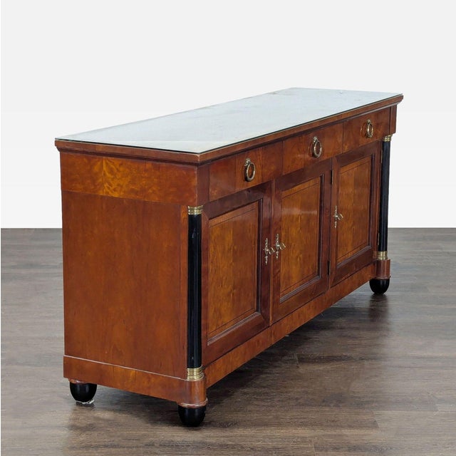 Carved cherry wood, with ebonized columns and feet, original brass hardware, and a glass protective top. The sideboard has...