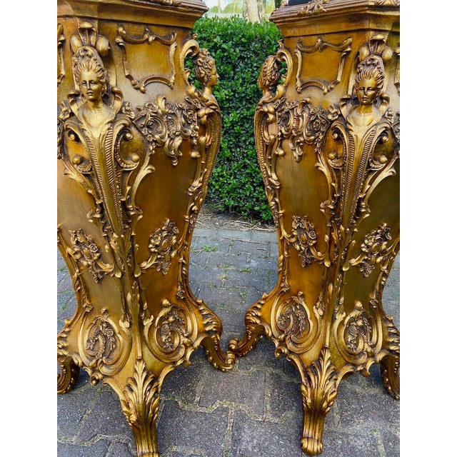 A decorative pair of 1990s Italian Baroque-style pedestals, crafted in resin with a rich gilded finish and dark marble-...