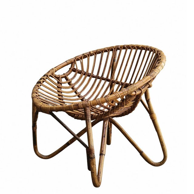 A low armchair for the living room or outdoor use featuring sturdy, hot-bent bamboo canes and crossed legs, a wide, shell-...