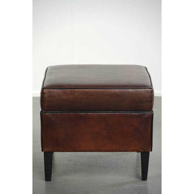This sheepskin ottoman features a beautiful dark color scheme and is finished with black piping. A footstool, also known...