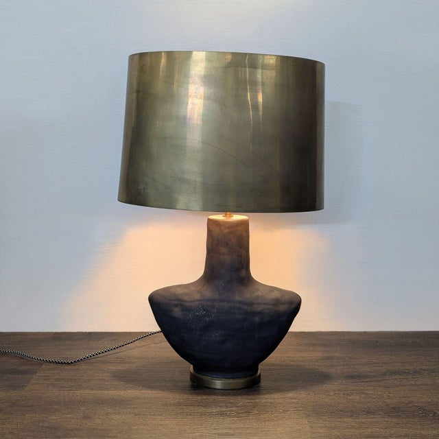This Visual Comfort table lamp features a stylish matte black base with a unique sculptural shape and a sleek brass shade....