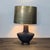 This Visual Comfort table lamp features a stylish matte black base with a unique sculptural shape and a sleek brass shade....