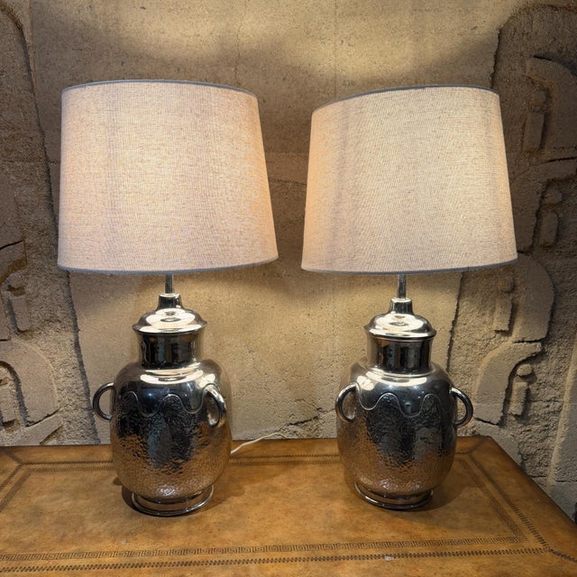 For your consideration, a pair of hammered metal table lamps with a shiny silver or polished chrome finish. The design...