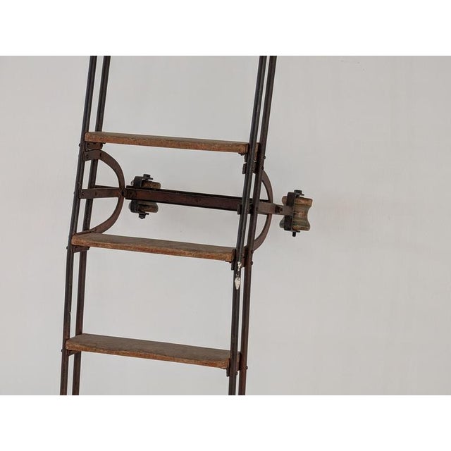 A massive antique library ladder, approximately 3 meters high, crafted from steel with solid wood steps. The ladder rolls...