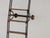 A massive antique library ladder, approximately 3 meters high, crafted from steel with solid wood steps. The ladder rolls...