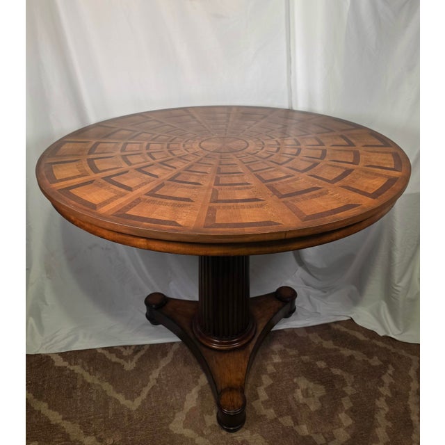 An exceptional round pedestal dining table by luxury furniture maker Theodore Alexander, featuring an intricately...