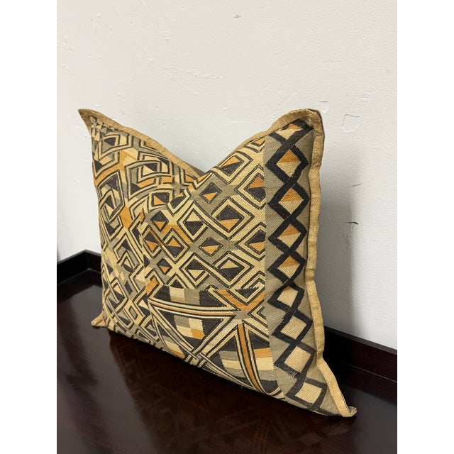 Design Plus Gallery presents a Kuba Cloth Geometric Decorative Pillow. Kuba cloth in olive, black, cream, and ochre forms...