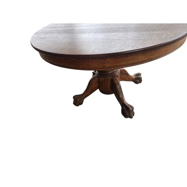 Antique American quarter-sawn oak dining table featuring a substantial pedestal base terminating in carved claw feet. The...