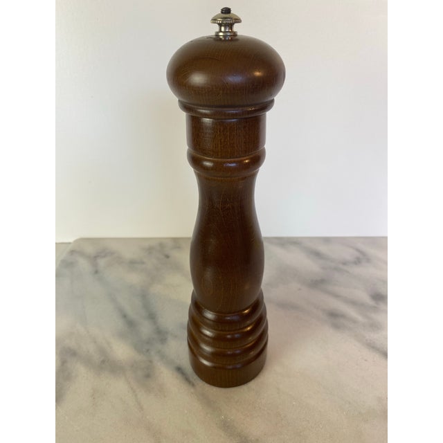A mid-century wooden Peugeot pepper mill with a gently curved silhouette and warm brown finish. The top is fitted with a...