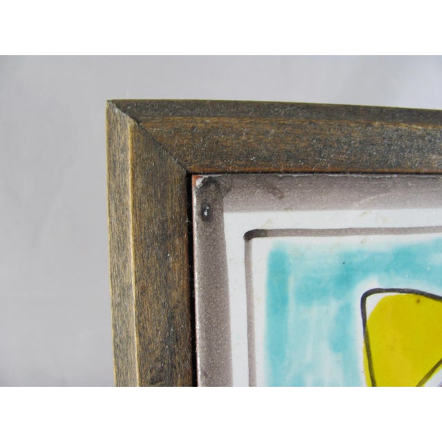 This wood framed tile was used as wall art, and still has the claw picture hanger with two felt pads on the back in the...