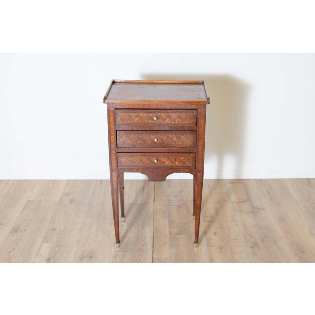 A charming Louis XVI-style bedside table adorned with intricate geometric marquetry and a floral inlay decoration on the...