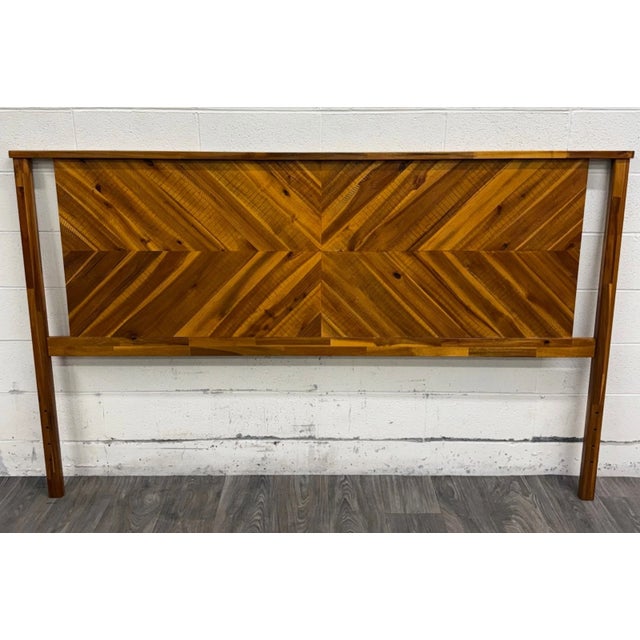 This is a modern king headboard crafted from solid acacia wood with a striking geometric chevron pattern in warm golden...