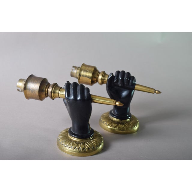 Matching pair of Art Deco wall sconces from the 1930s, each formed as a fist holding a torch, in solid brass with a dark...
