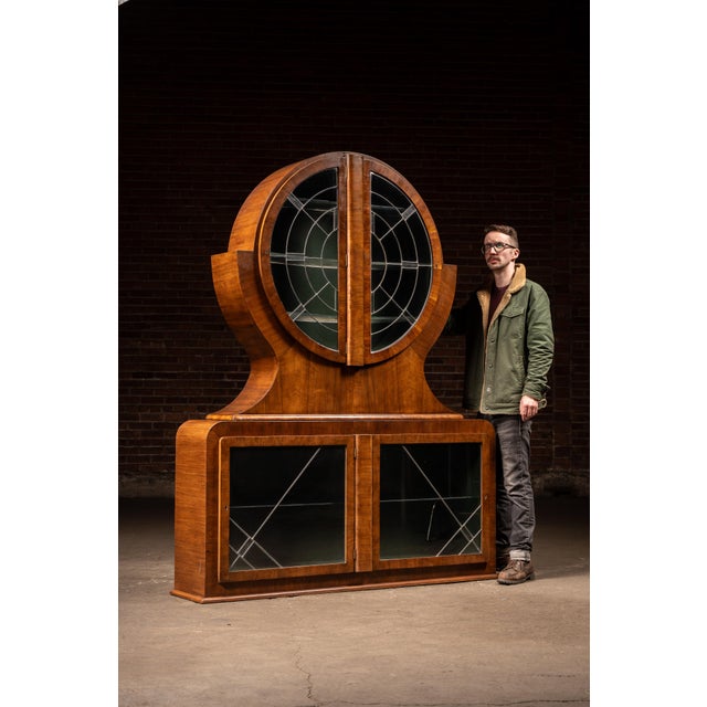 Striking two-part liquor cabinet defined by its dramatic circular upper case, framed in richly figured walnut with a warm,...