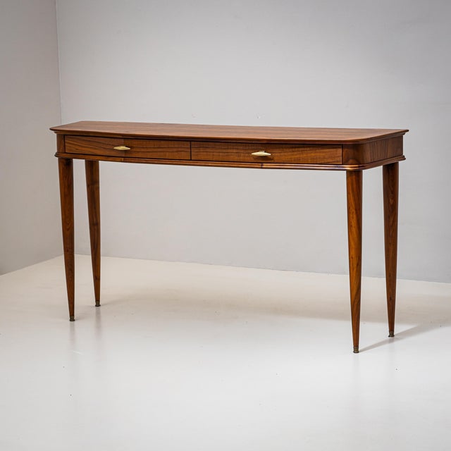 Walnut console table with two drawers and tall tapered legs. The handles are made of brass. The slightly bowed console has...