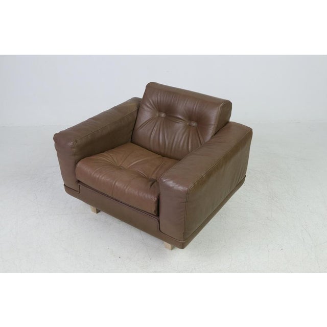 Vintage armchair upholstered in brown leather with legs of stained wood, equipped with a loose seat cushion.